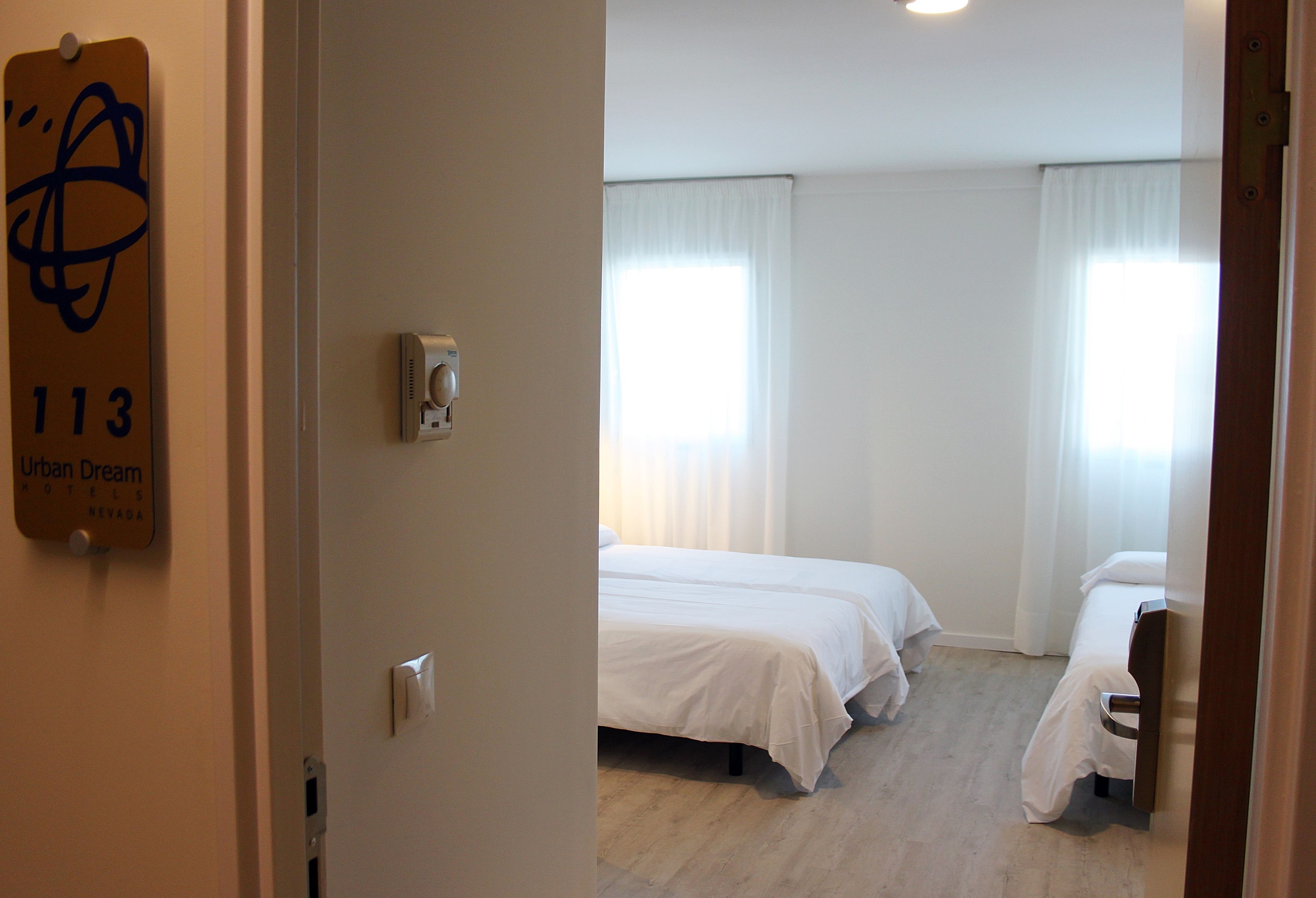 Habitación de hotel con dos camas, un termostato y una ventana con cortinas.