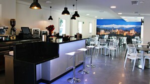 Una cafeteria moderna amb zona de bar, seients i un mural amb un paisatge urbà a la paret.