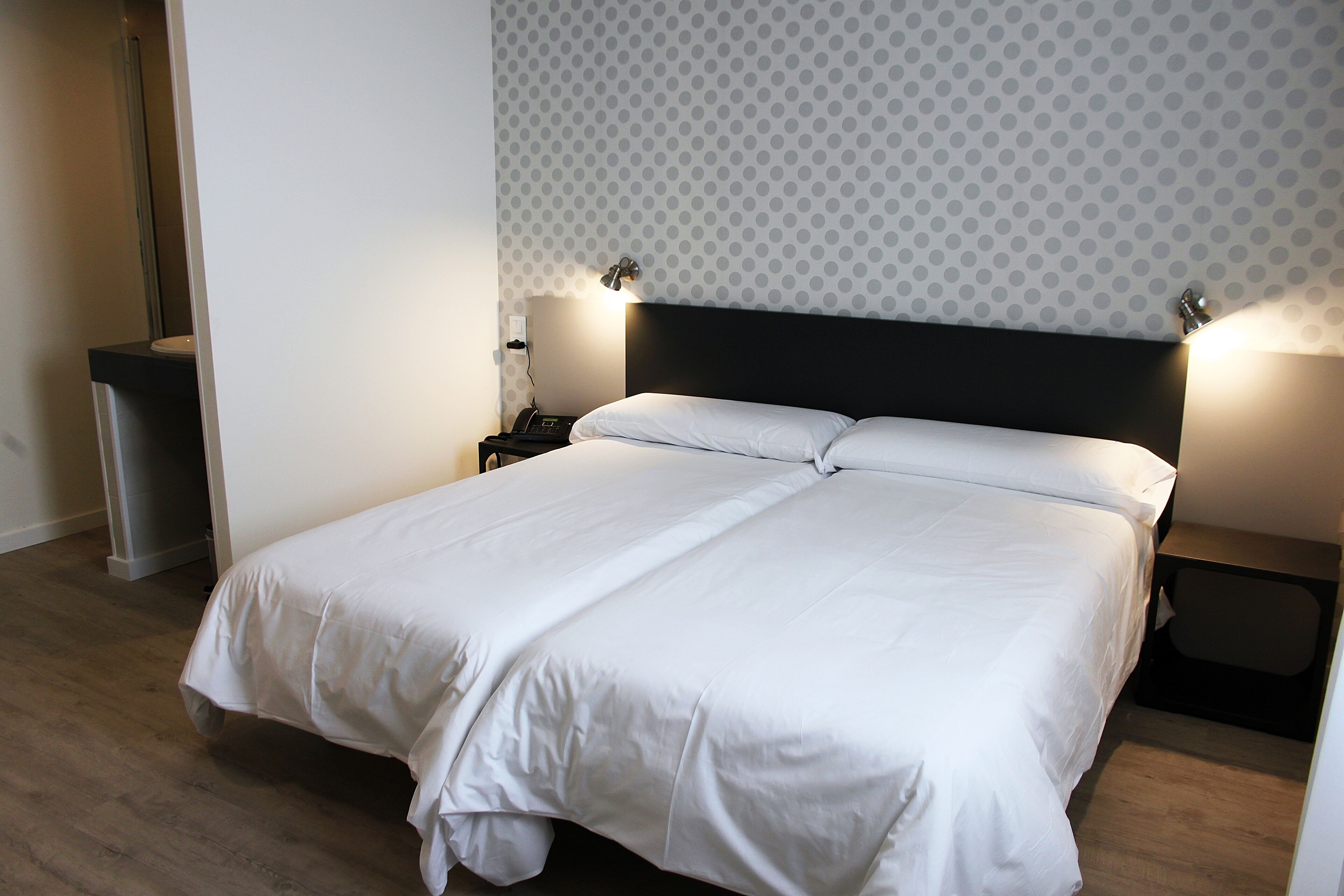 A neatly made double bed with white linens, a modern headboard, and two bedside lamps.