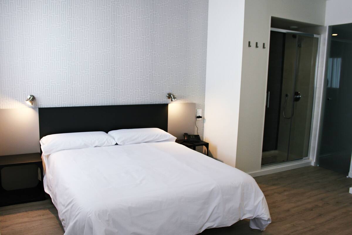 A neatly made bed with white linens, a dark headboard, and two bedside lamps.