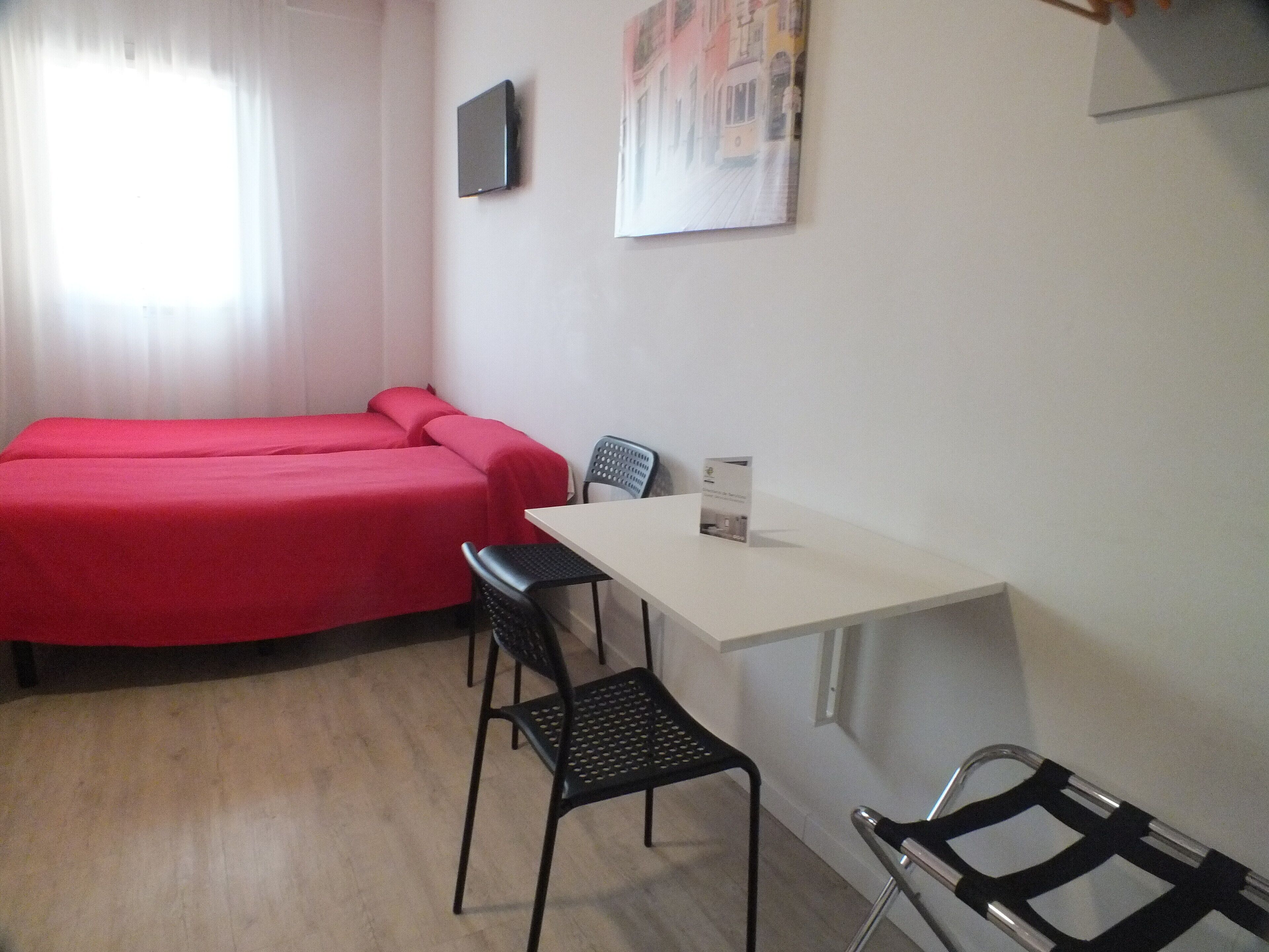 A room with two beds, a table, two chairs, a TV, and a painting on the wall.