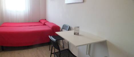 A room with two beds, a table, two chairs, a TV, and a painting on the wall.