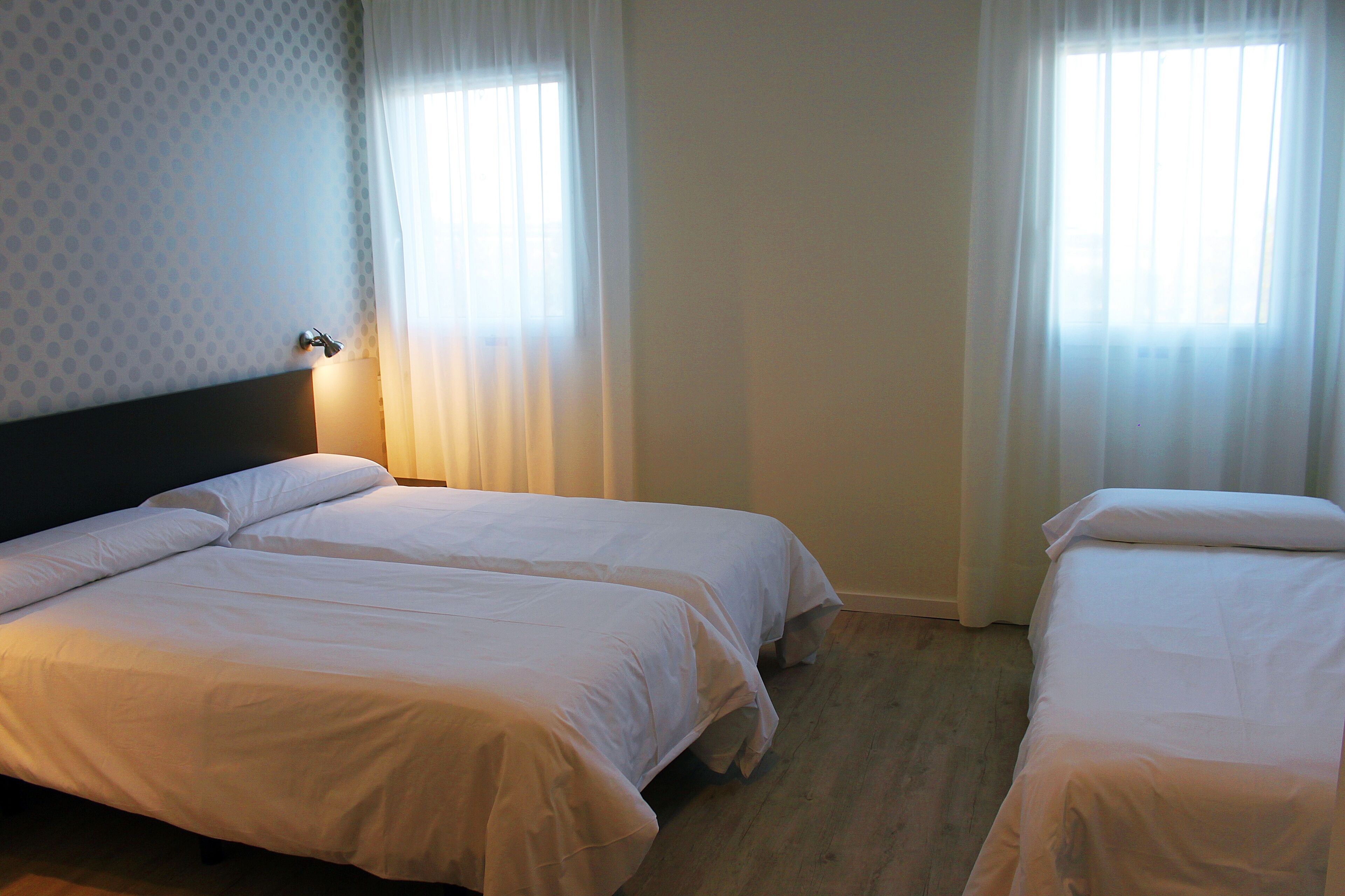 Habitación de hotel con dos camas individuales, cabecera y ventana con cortinas.