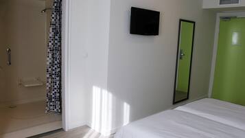 Habitació d'hotel amb dutxa, un llit, televisió i una porta verda.