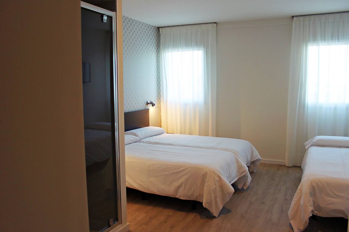 A hotel room with two single beds, a wooden floor, and a door leading to another room.