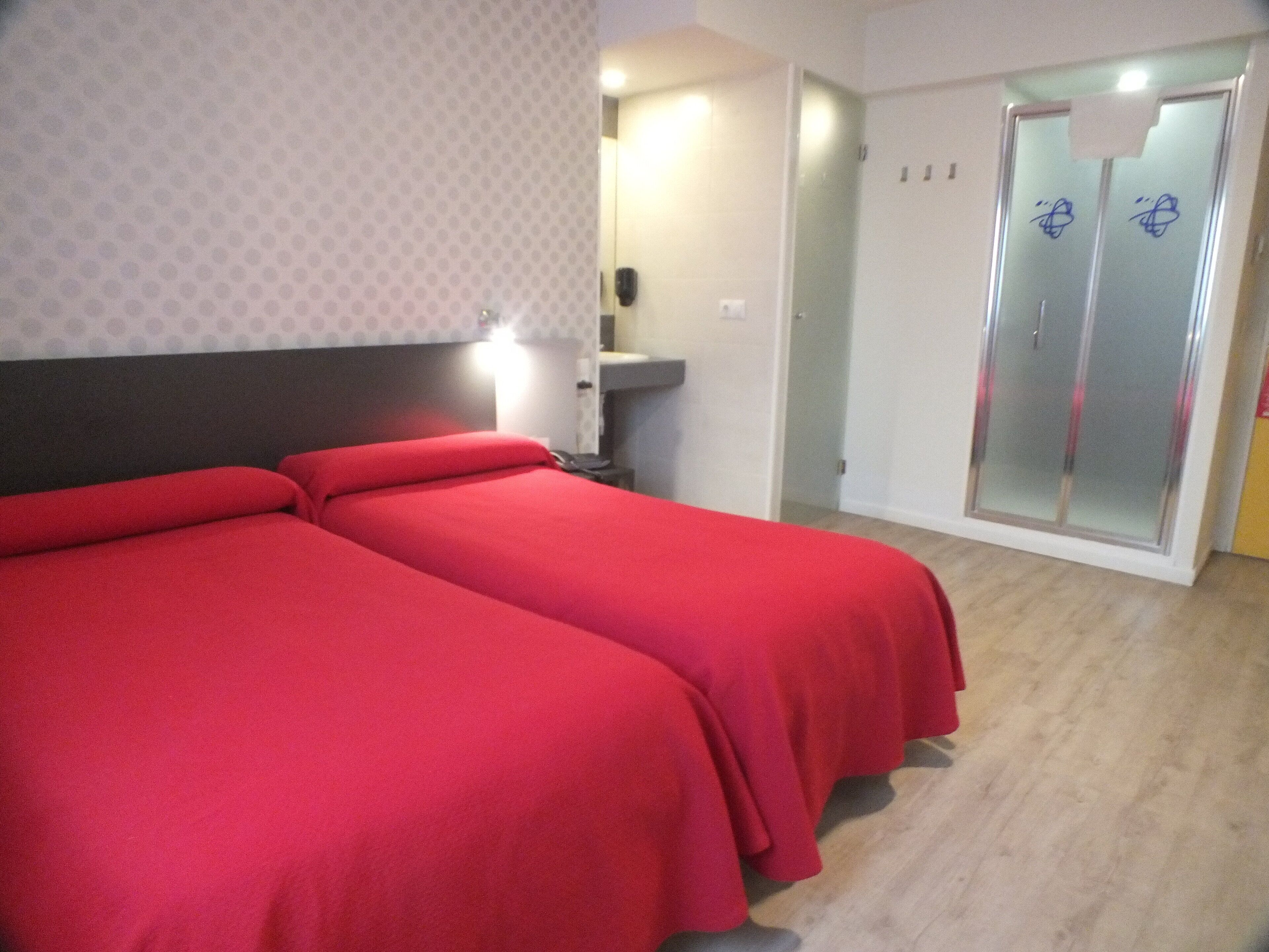 Een hotelkamer met twee eenpersoonsbedden, een badkamer met een glazen douchedeur en een klein bureau met een stoel.