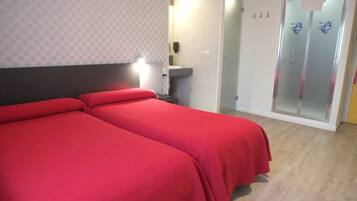 Een hotelkamer met twee eenpersoonsbedden, een badkamer met een glazen douchedeur en een klein bureau met een stoel.