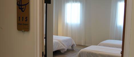 Een hotelkamer met twee bedden, een deur met een bordje en een raam met gordijnen.
