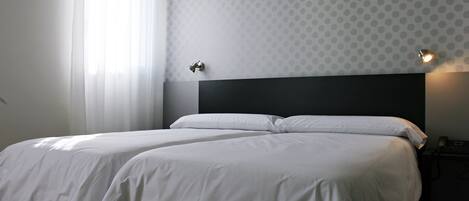 A hotel room with two beds, a nightstand, and a wall-mounted lamp.