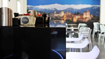 A hotel reception area with a modern counter, a coffee machine, and a view of a cityscape with mountains in the background.