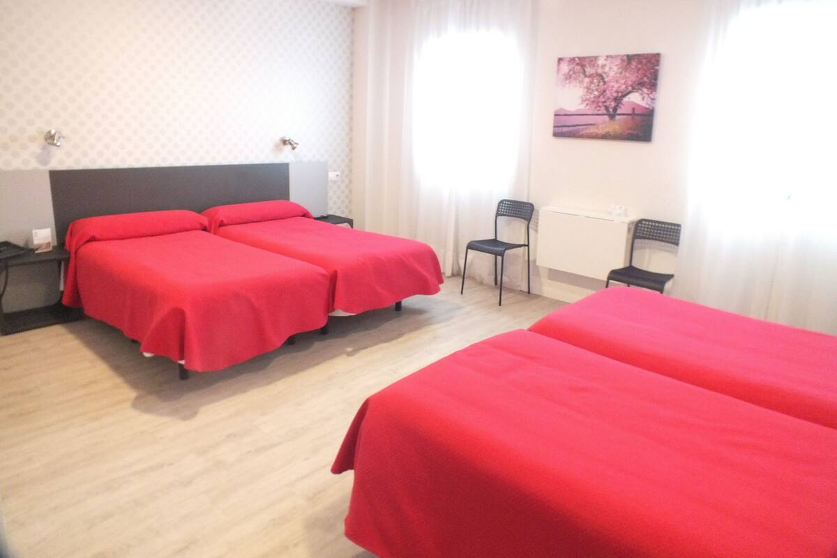 A hotel room with two beds, a desk, a chair, and a window with curtains.