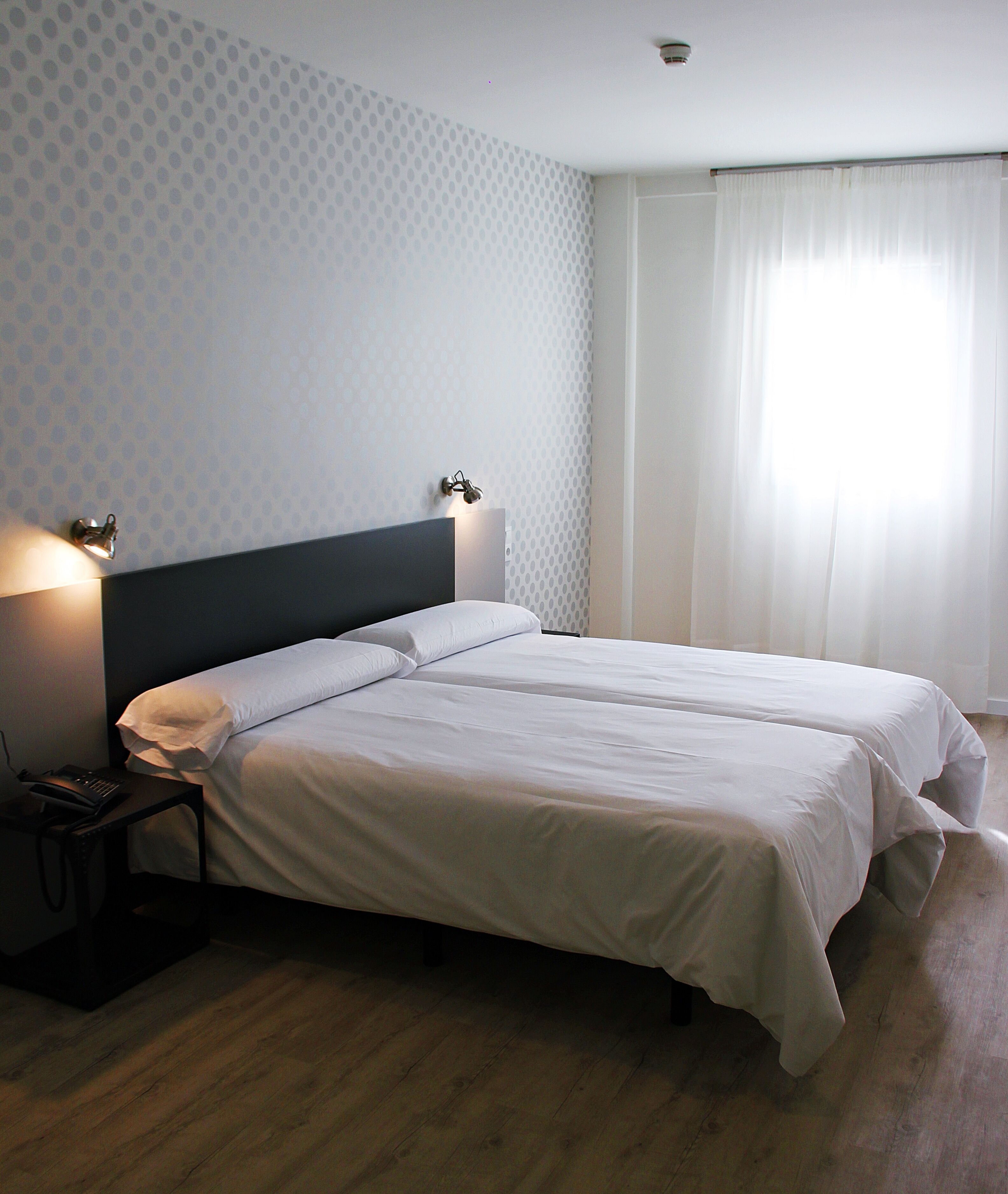 A neatly made double bed with white linens, a dark headboard, and two bedside lamps.