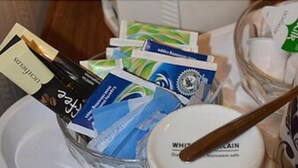 A tray with a white mug, a spoon, and various packaged items including coffee and tea. - Abbey Lodge (London)
