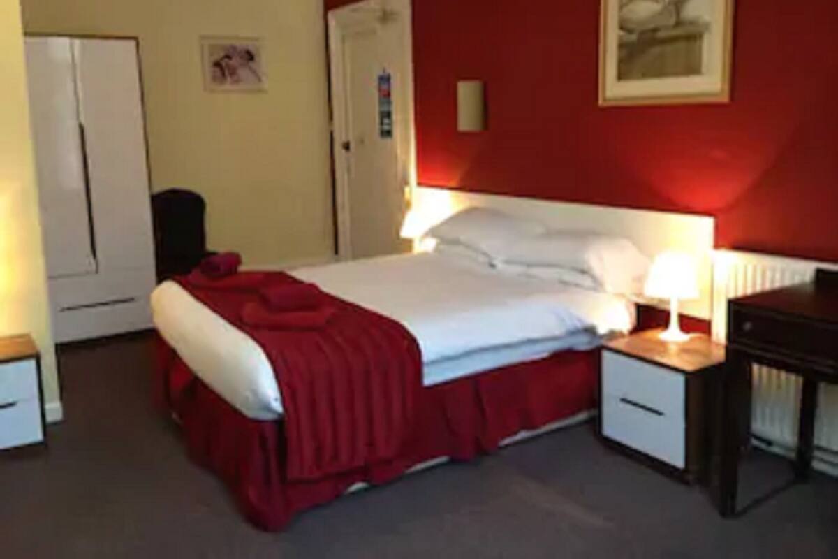 A hotel room with a bed, bedside tables, a desk, a chair, a wardrobe, and a painting on the wall.