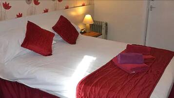 A hotel room with a bed, red pillows, a bedside lamp, and a folded towel on the bed.
