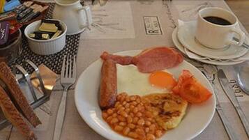 A breakfast plate with eggs, beans, tomatoes, and bacon, accompanied by a cup of coffee and cutlery on a table.