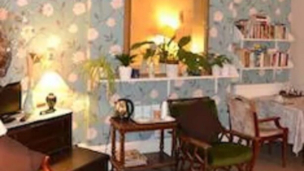 A room with floral wallpaper, a mirror, a bookshelf, and a desk with a lamp. - Abbey Lodge (London)
