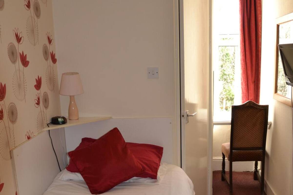A hotel room with a bed, a chair, a desk, a lamp, and a window with curtains.