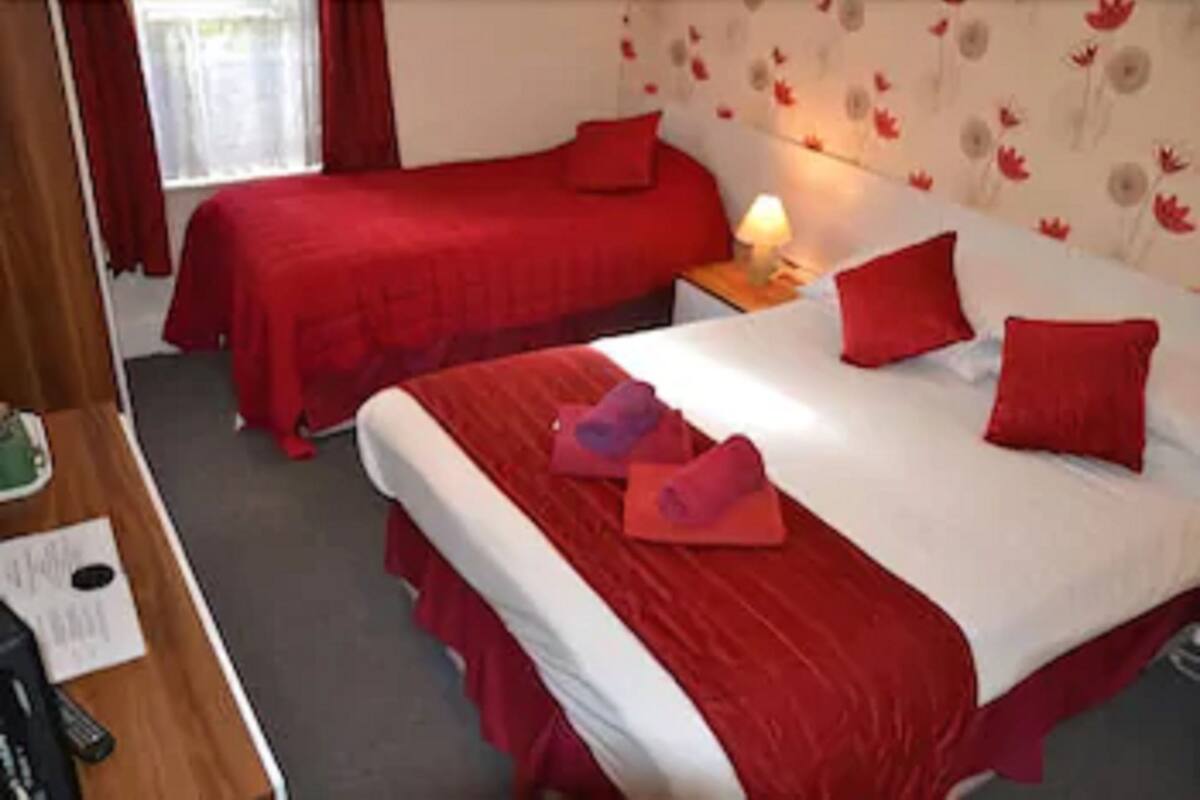 A hotel room with two beds, red bedding, a nightstand with a lamp, and a floral wallpaper.