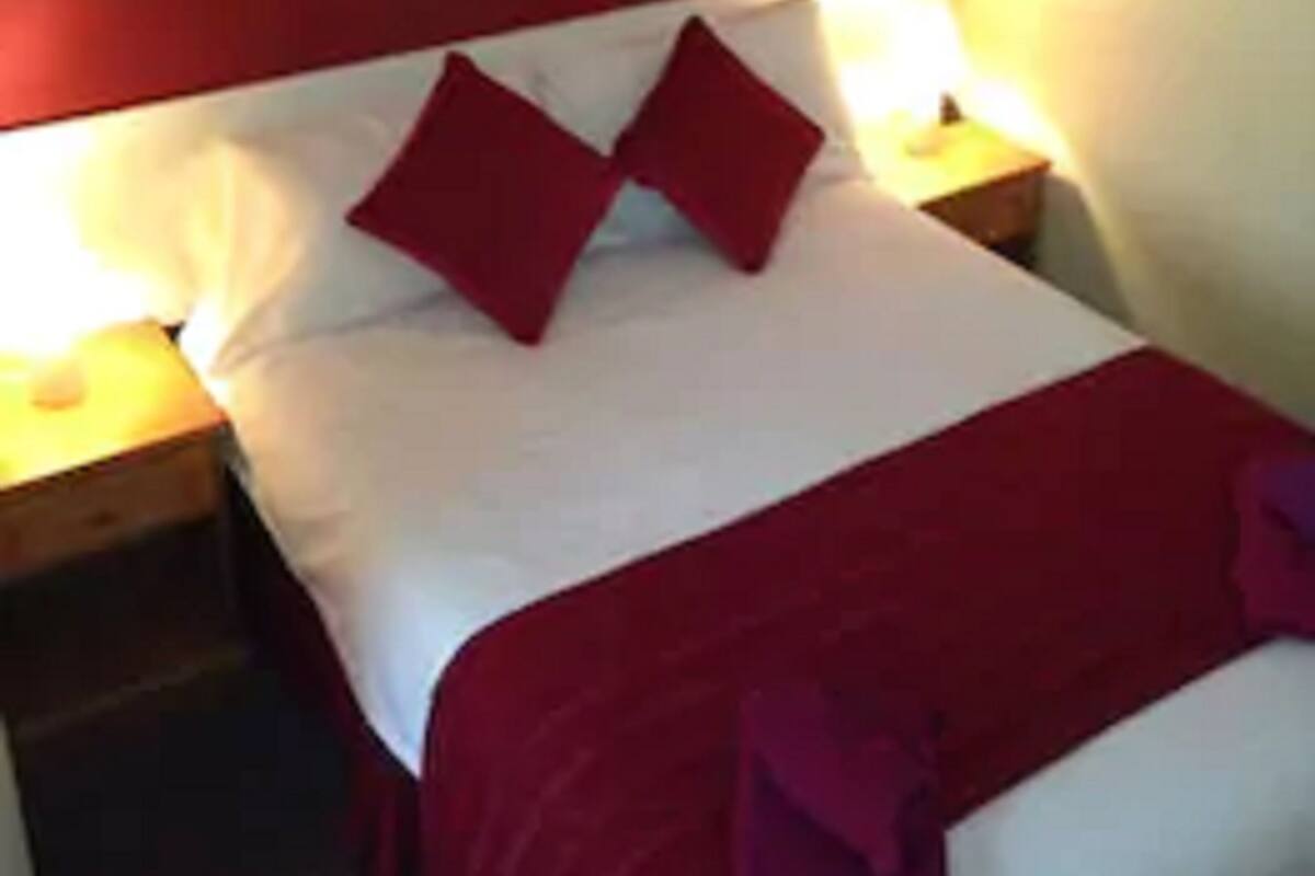 A bed with a red headboard, two red pillows, and a white bedspread. There is a framed picture on the wall above the bed.