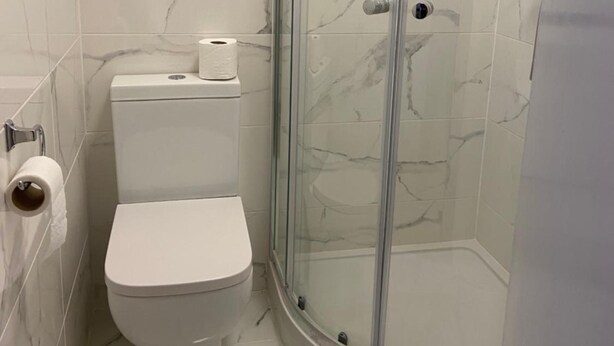 Ein Badezimmer mit Duschkabine, Toilette und Wänden mit Marmoroptik.