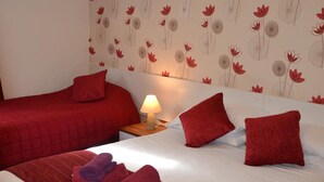 A hotel room with two beds, red bedding, a nightstand with a lamp, and a floral wallpaper design. - Abbey Lodge (London)