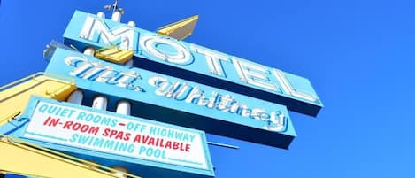 A motel sign with 'MOTEL' and 'The Whitney' written on it, along with amenities like quiet rooms, off highway in-room spas, and a swimming pool.