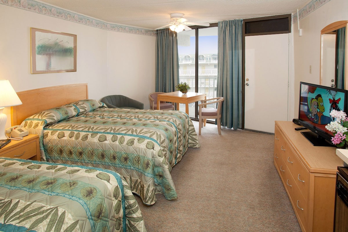 A hotel room with two beds, a desk, a chair, a television, and a window with curtains.
