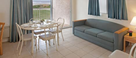 A dining area with a table set for four, a sofa, and a view of the beach through a large window.