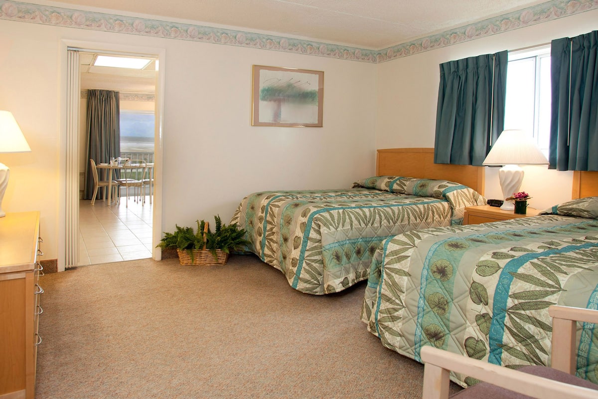 A hotel room with two beds, a dining area with a table and chairs, a TV, and a view of the outdoors.