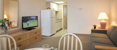 A dining area with a table set for two, a television, a refrigerator, and a sofa.