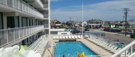 A hotel with a swimming pool, multiple balconies, and a view of the street.