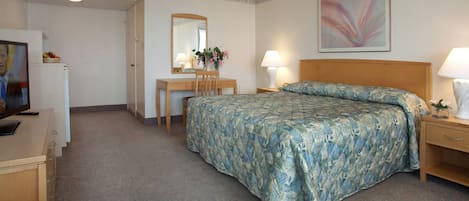 A hotel room with a bed, a desk, a chair, a television, and a lamp.
