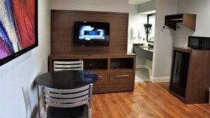 A modern kitchen with a built-in TV, wooden cabinets, a dining area with a round table and chairs, and a microwave. - Palace Inn - Antoine (Houston)