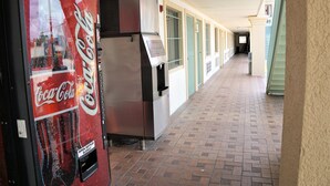 A corridor with a Coca-Cola vending machine and a refrigerator. - Palace Inn - Antoine (Houston)