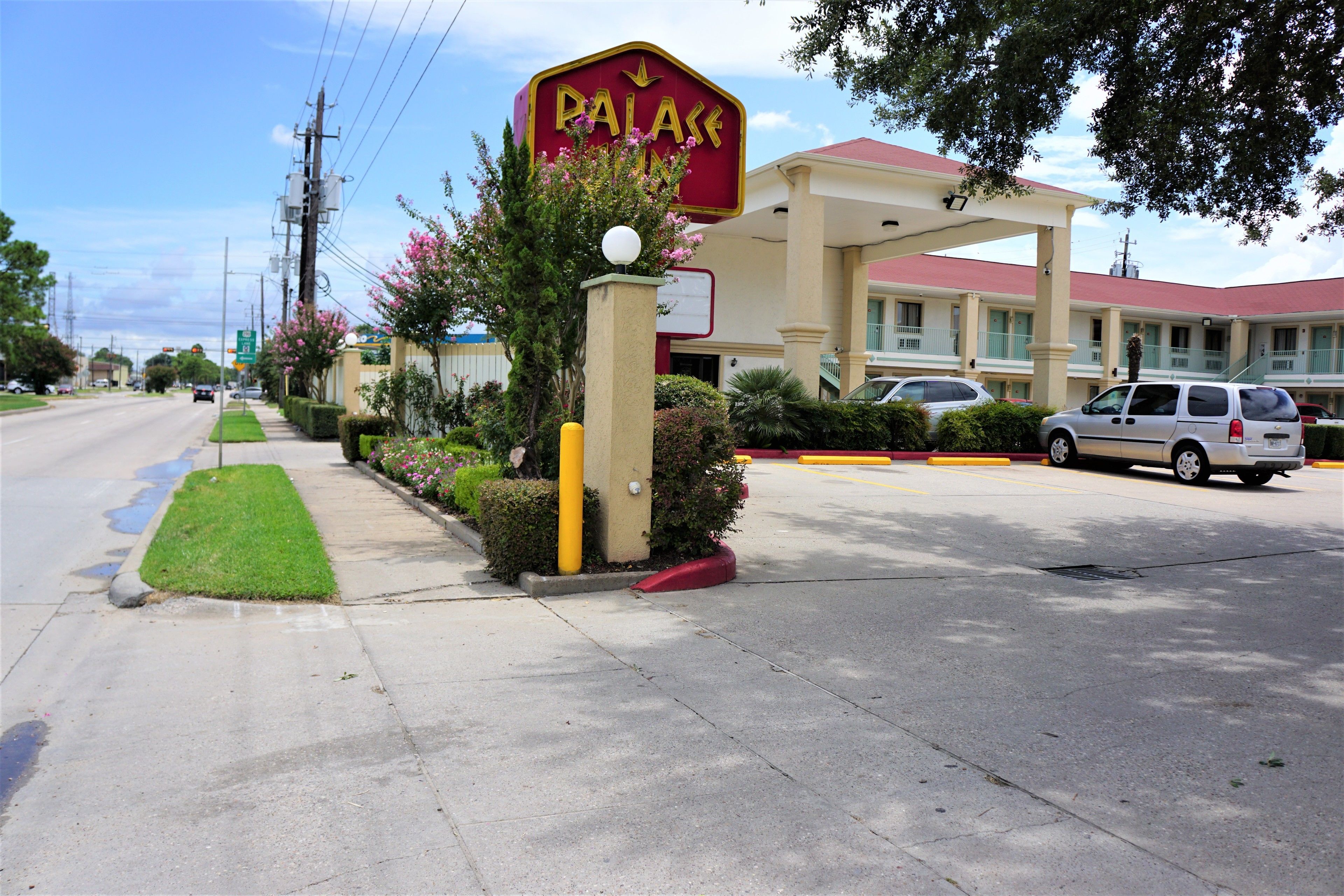 A hotel named "PALACE" with a red and yellow sign, a parking lot, and a building with a red roof.