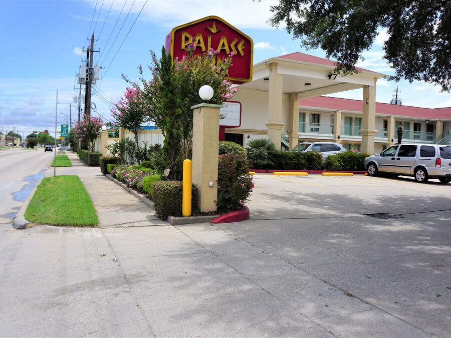 A hotel named "PALACE" with a red and yellow sign, a parking lot, and a building with a red roof.