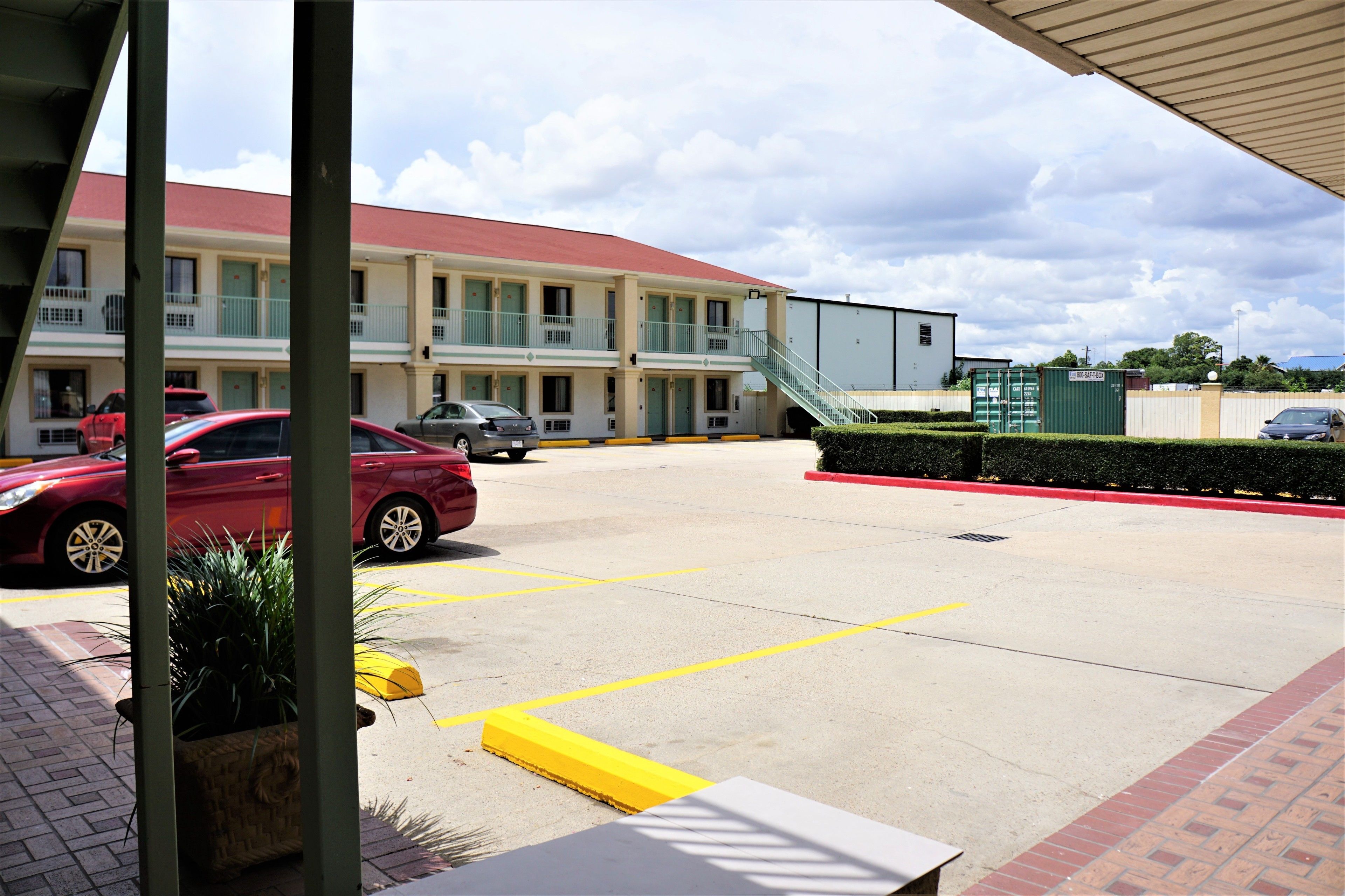 A parking lot with marked spaces, a building with a red roof, and a staircase leading to a green container.