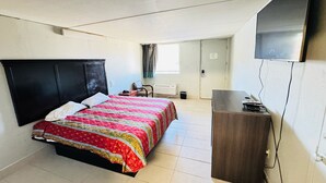 Una habitación de hotel pequeña con cama, escritorio, televisor y ventana con cortinas.