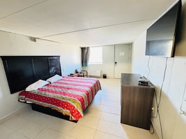 A compact hotel room with a bed, a desk, a television, and a window with curtains.