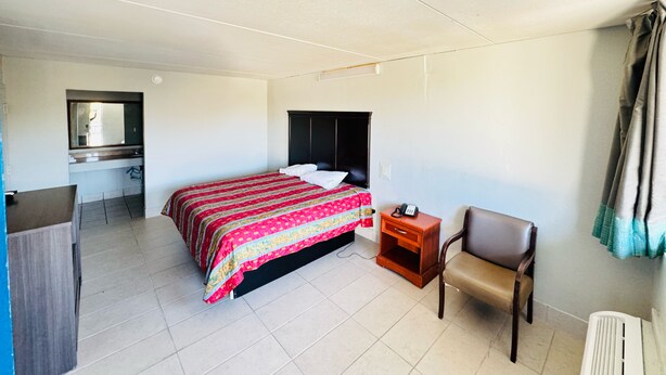 Una habitación de hotel con cama, mesita de noche, silla, escritorio y espejo.
