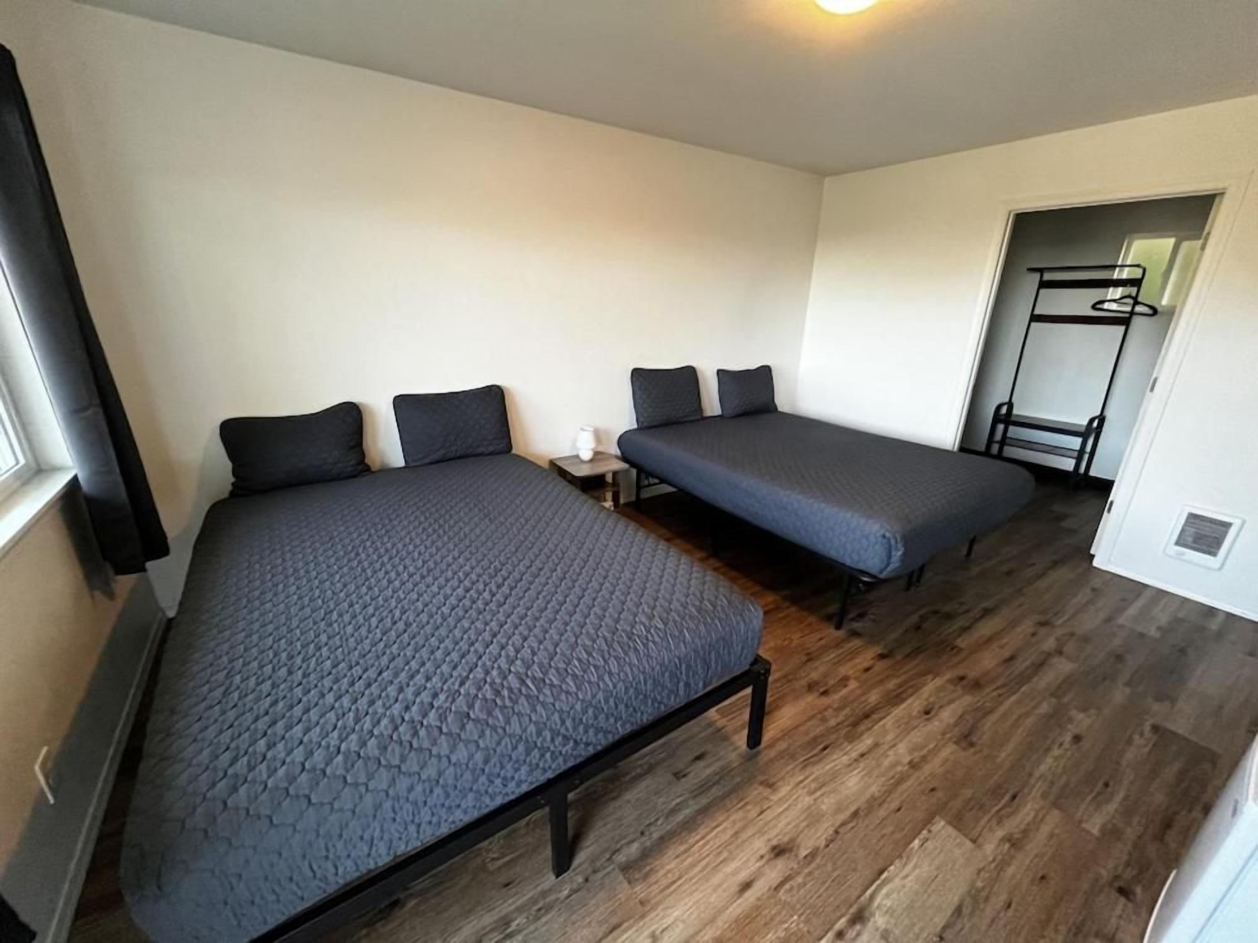 Una habitación con dos camas, una mesita de noche pequeña, una silla y un perchero.