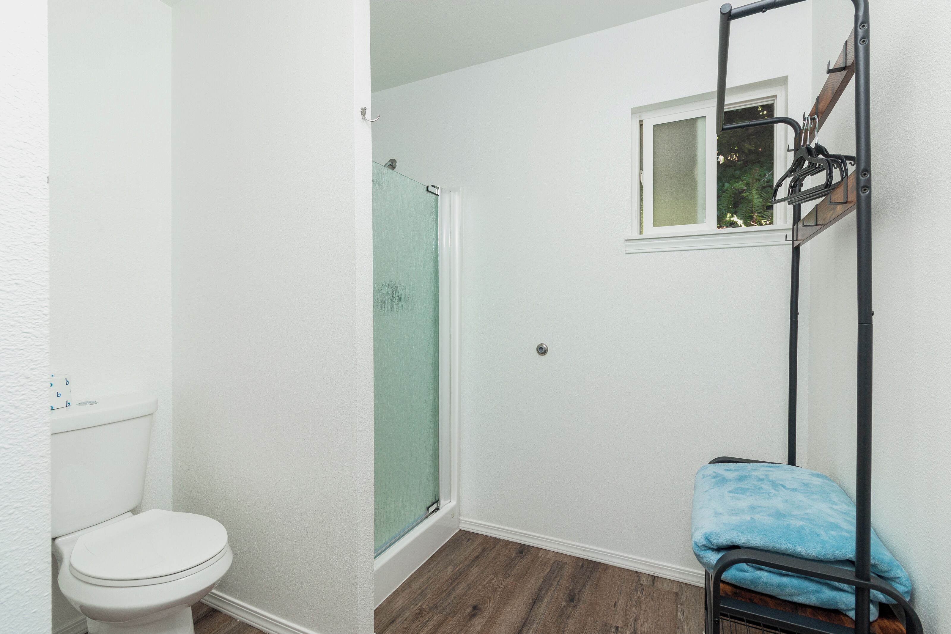 A bathroom with a toilet, a glass shower enclosure, and a metal rack with a blue towel.