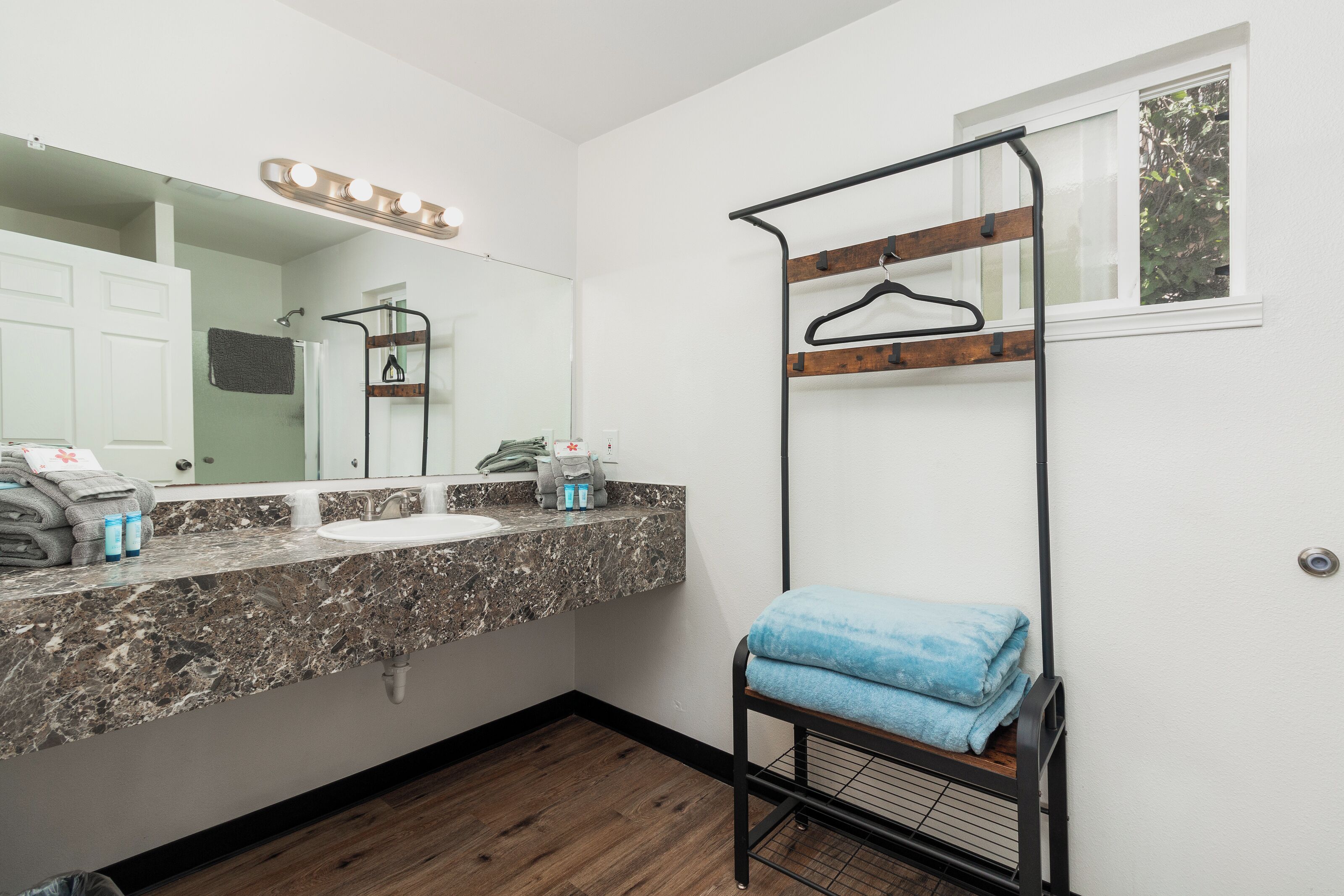 A bathroom with a marble countertop, a sink, a mirror, a towel rack, and a window.