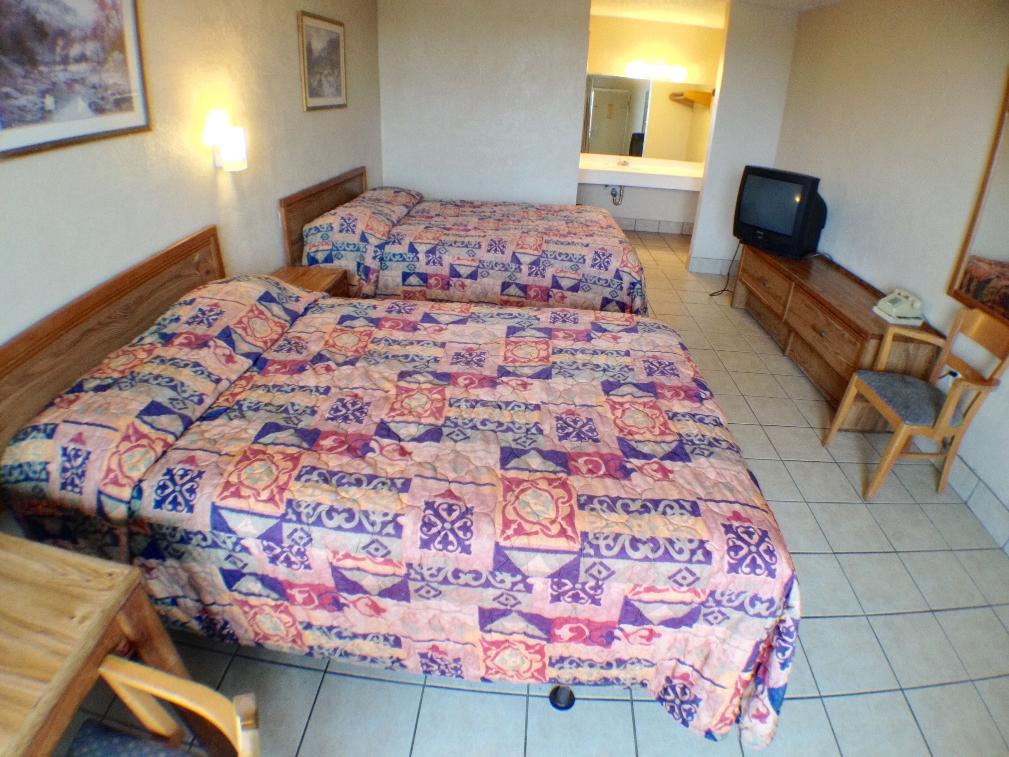A hotel room with two beds, a television, a wooden dresser, and a small table.