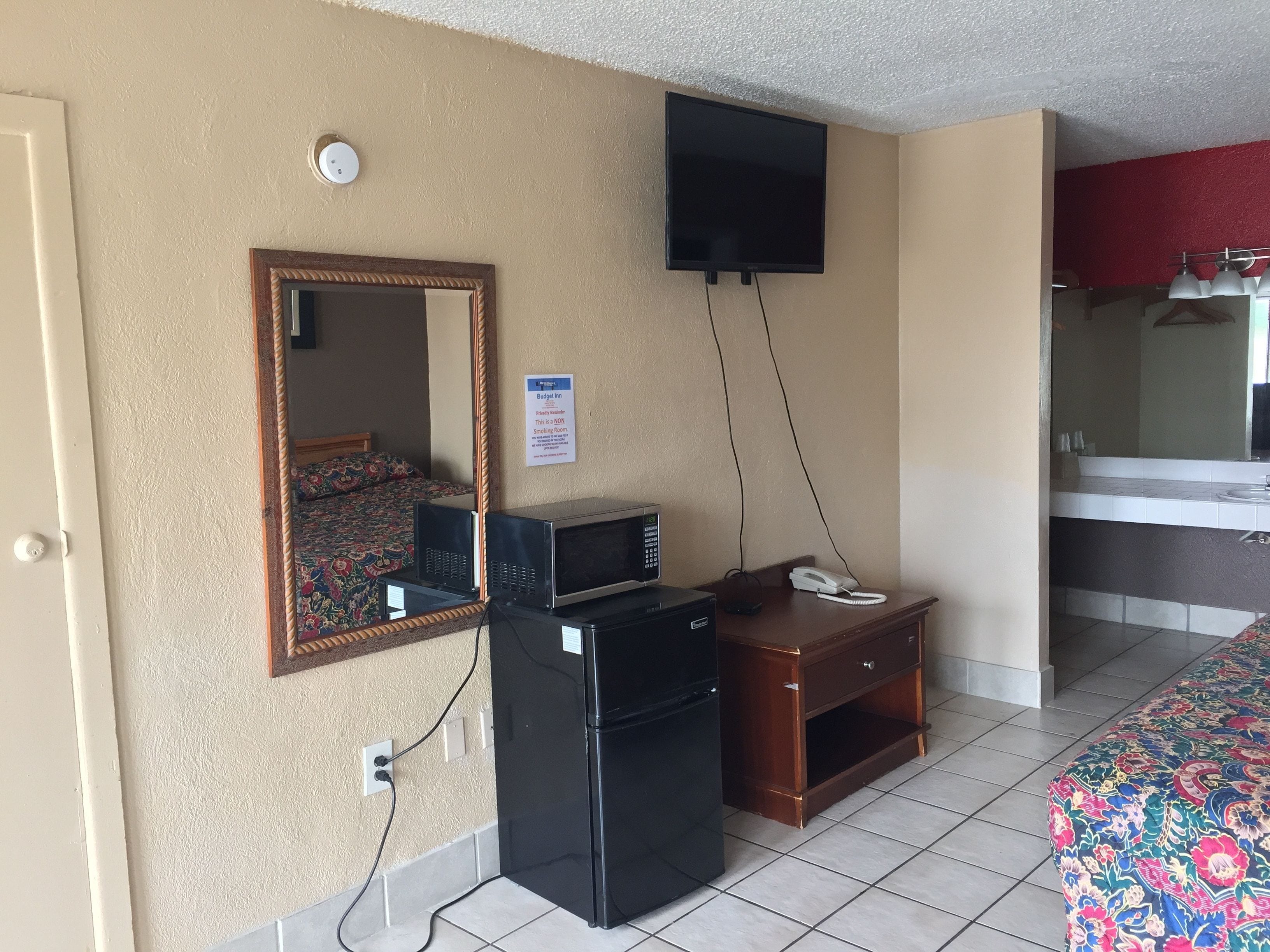 Una habitación de hotel con una cama, un escritorio con teléfono, microondas, televisor y espejo.