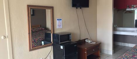 Una habitación de hotel con una cama, un escritorio con teléfono, microondas, televisor y espejo.