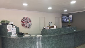 Un espace d’accueil avec un comptoir en marbre, une horloge, un téléviseur et une guirlande décorative accrochée au mur.