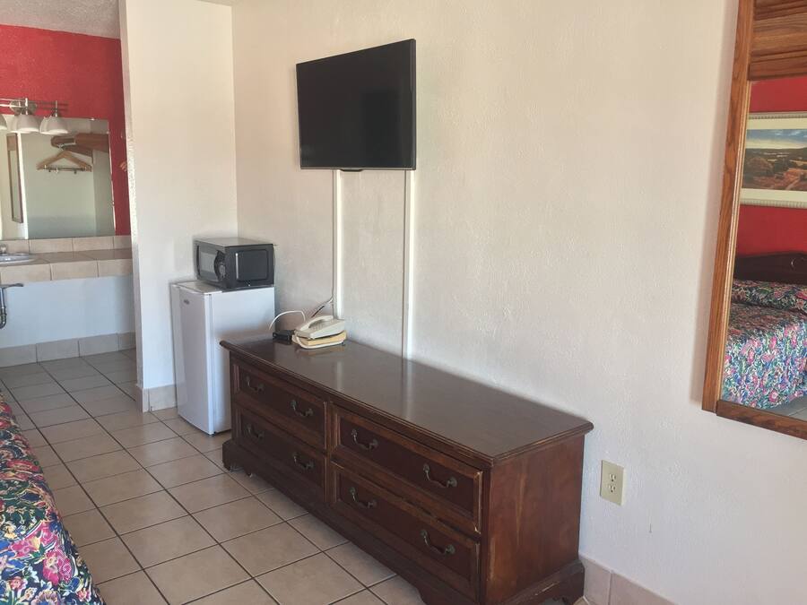 A bedroom with a bed, a dresser, a television mounted on the wall, a microwave, and a telephone.