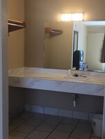 A bathroom with a white marble countertop, a sink, a mirror, and a light fixture above the mirror.